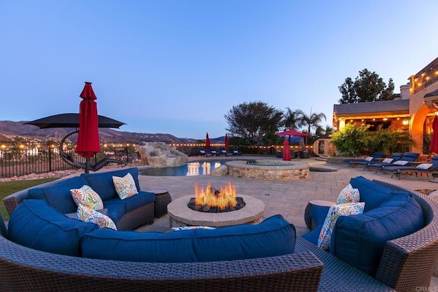 view of patio / terrace with a mountain view, an outdoor living space with a fire pit, an in ground hot tub, and fence