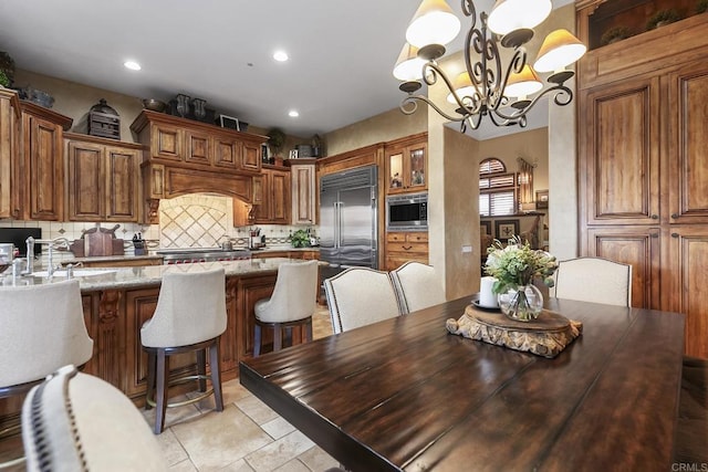 kitchen featuring a sink, built in appliances, tasteful backsplash, brown cabinets, and a chandelier