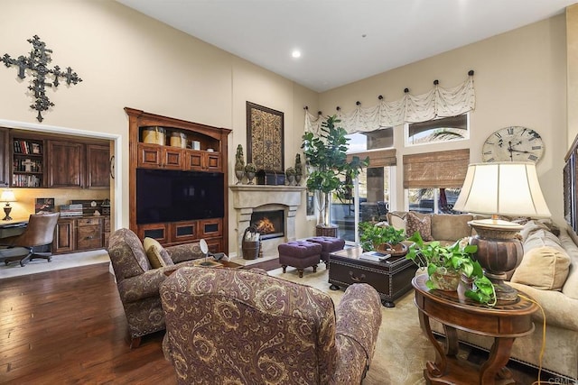 living area featuring hardwood / wood-style flooring, a high ceiling, a lit fireplace, and built in study area