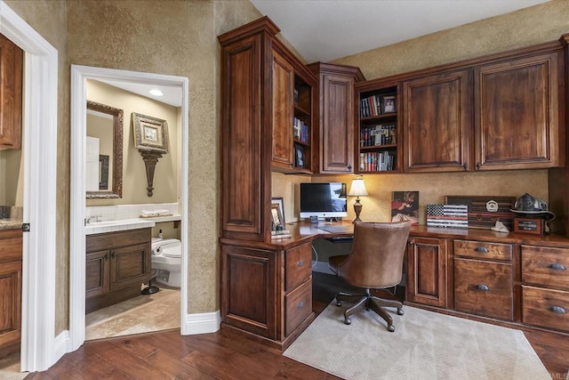 office space featuring dark wood finished floors, built in study area, baseboards, and a textured wall