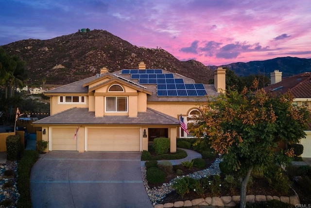 view of front of home featuring solar panels, an attached garage, stucco siding, driveway, and a mountain view