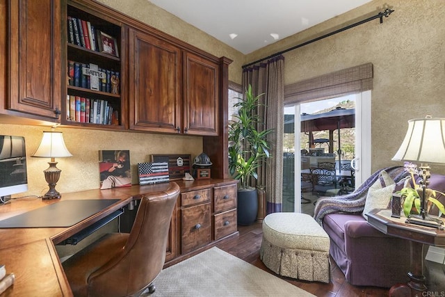 home office featuring dark wood finished floors, built in desk, and a textured wall