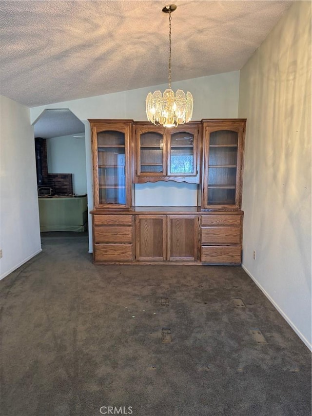 unfurnished dining area featuring a chandelier, dark carpet, a textured ceiling, and baseboards