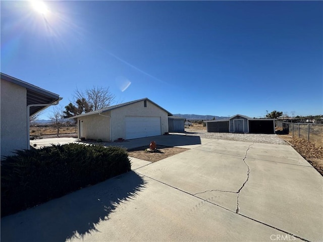 exterior space featuring driveway, an outdoor structure, fence, stucco siding, and a storage unit