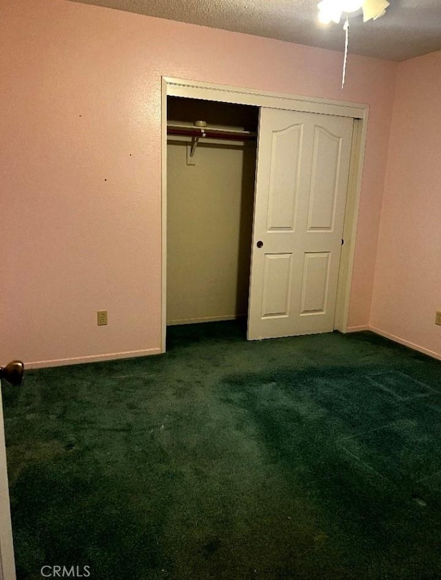 unfurnished bedroom with a textured ceiling, dark colored carpet, a closet, and baseboards