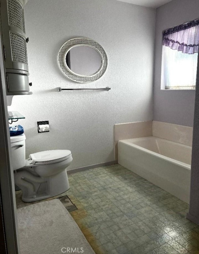 bathroom featuring a garden tub, toilet, tile patterned floors, and baseboards