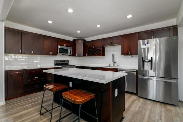 kitchen with a kitchen breakfast bar, appliances with stainless steel finishes, light wood-type flooring, a kitchen island, and sink