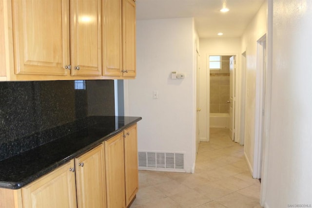 kitchen featuring light brown cabinetry, dark stone countertops, light tile patterned floors, and decorative backsplash