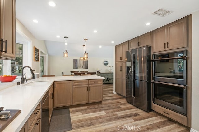 kitchen with pendant lighting, kitchen peninsula, sink, light hardwood / wood-style flooring, and appliances with stainless steel finishes