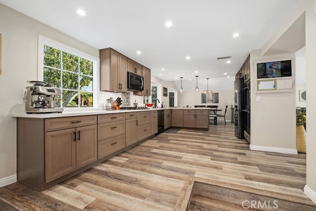 kitchen featuring pendant lighting, light hardwood / wood-style flooring, kitchen peninsula, and black appliances