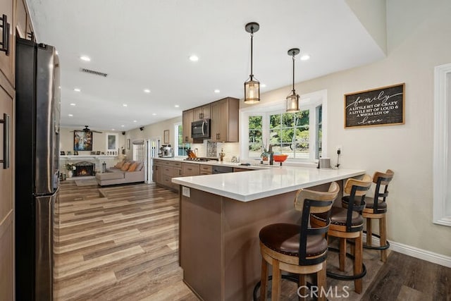 kitchen with hardwood / wood-style floors, a breakfast bar, kitchen peninsula, hanging light fixtures, and stainless steel appliances