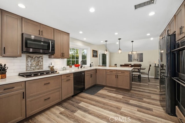 kitchen featuring decorative light fixtures, backsplash, hardwood / wood-style floors, black appliances, and kitchen peninsula