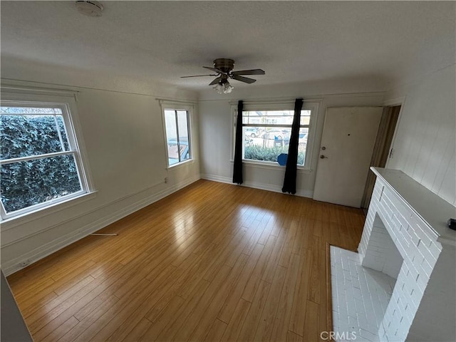 unfurnished living room with light wood-type flooring, ceiling fan, and a brick fireplace