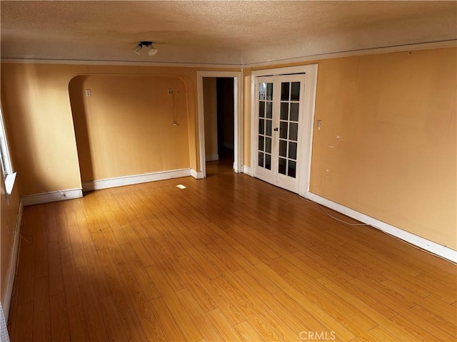 empty room with a textured ceiling, light hardwood / wood-style flooring, and french doors