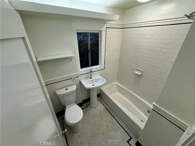 bathroom featuring toilet, tile patterned flooring, tile walls, and tiled shower / bath