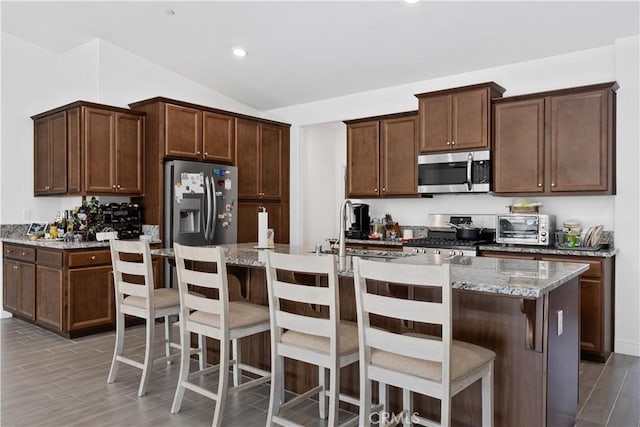 kitchen featuring stainless steel appliances, an island with sink, light stone countertops, and a kitchen breakfast bar