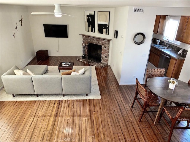 living room featuring visible vents, baseboards, a fireplace, wood finished floors, and a ceiling fan