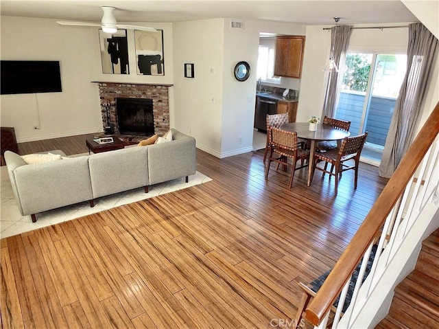 living area with light wood finished floors, visible vents, baseboards, a fireplace, and a ceiling fan