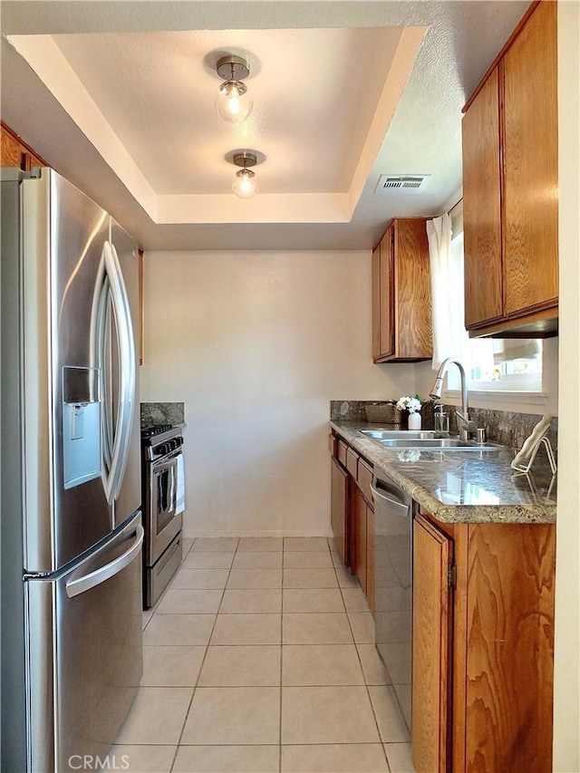 kitchen featuring a sink, a tray ceiling, brown cabinetry, and stainless steel appliances