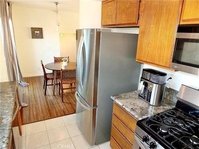 kitchen featuring light tile patterned flooring, stone countertops, hanging light fixtures, appliances with stainless steel finishes, and brown cabinets