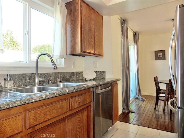 kitchen with tile patterned floors, brown cabinets, stainless steel appliances, and a sink