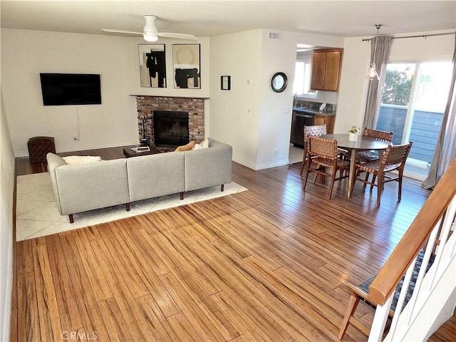 living room with visible vents, light wood-style flooring, a ceiling fan, baseboards, and a brick fireplace