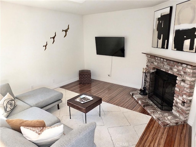 living area featuring a brick fireplace, baseboards, and wood finished floors