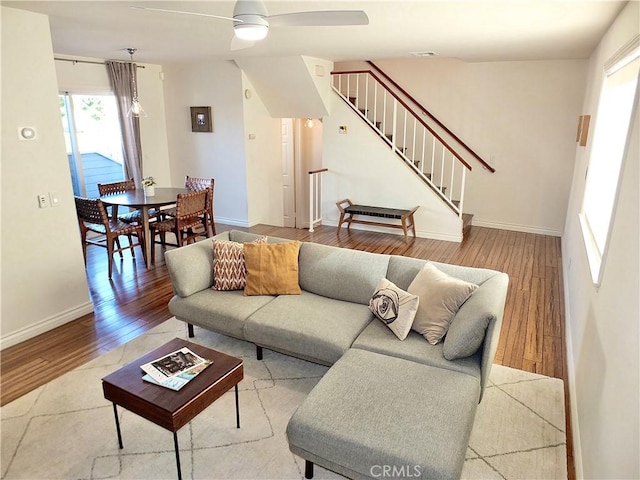 living area with a ceiling fan, stairway, wood finished floors, and baseboards