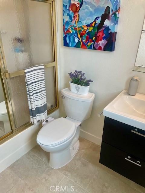 bathroom with enclosed tub / shower combo, toilet, vanity, and tile patterned flooring