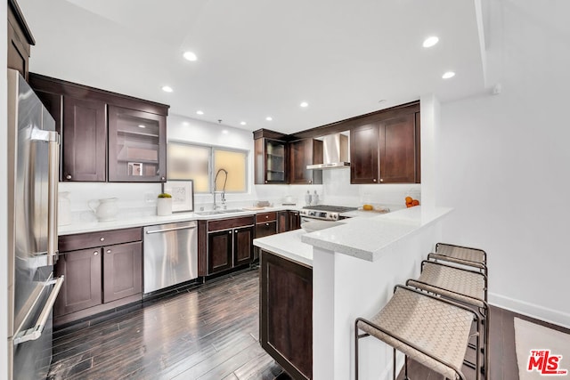 kitchen with appliances with stainless steel finishes, a kitchen breakfast bar, wall chimney range hood, and sink