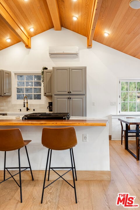 kitchen featuring a wall unit AC, light hardwood / wood-style flooring, tasteful backsplash, a kitchen breakfast bar, and sink