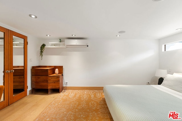 bedroom featuring french doors, light wood-type flooring, and an AC wall unit