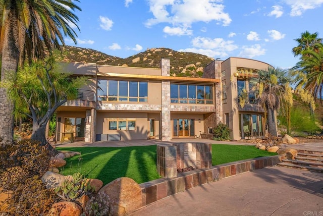 rear view of house with a patio, a mountain view, and a lawn