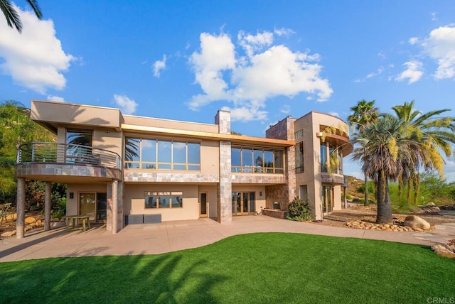 back of property featuring a balcony, a patio, and a lawn