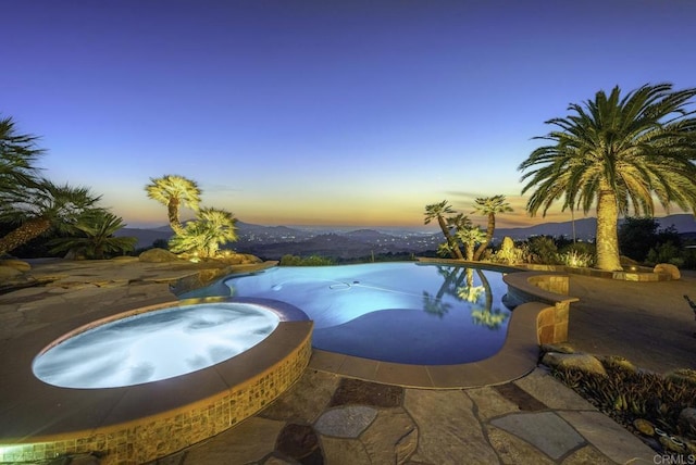 pool at dusk with an in ground hot tub and a mountain view