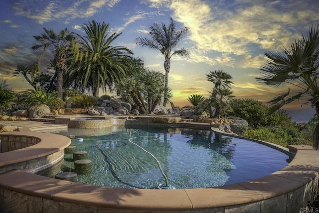 pool at dusk with an in ground hot tub