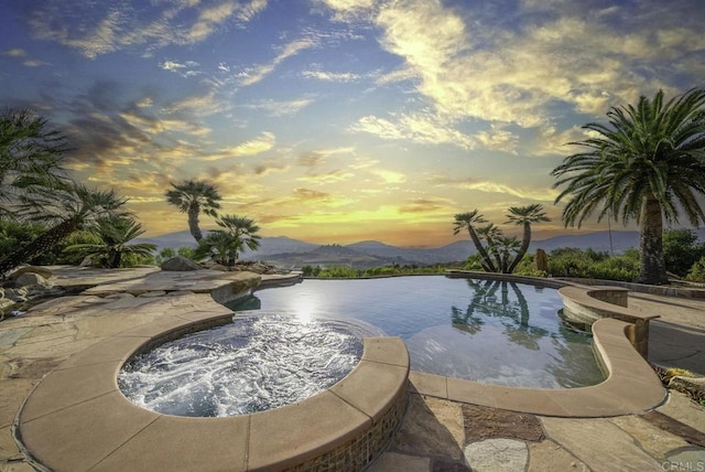 pool at dusk featuring an in ground hot tub and a water and mountain view