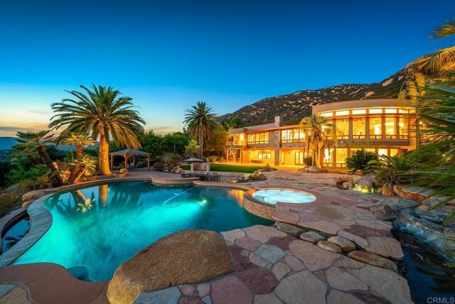 pool at dusk with a patio and an in ground hot tub