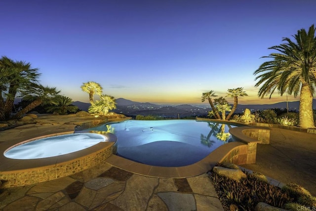 pool at dusk with a patio area, an in ground hot tub, and a mountain view