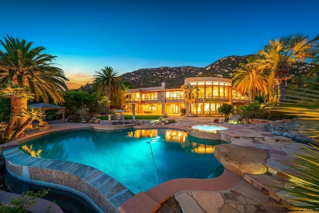 pool at dusk with a patio area, an in ground hot tub, and a mountain view