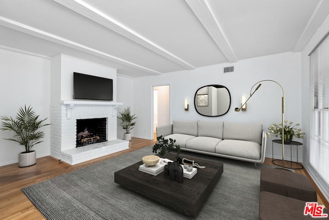 living room featuring a brick fireplace, beamed ceiling, and hardwood / wood-style floors