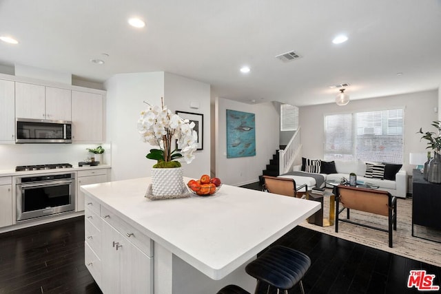 kitchen with white cabinets, stainless steel appliances, a center island, and dark hardwood / wood-style floors