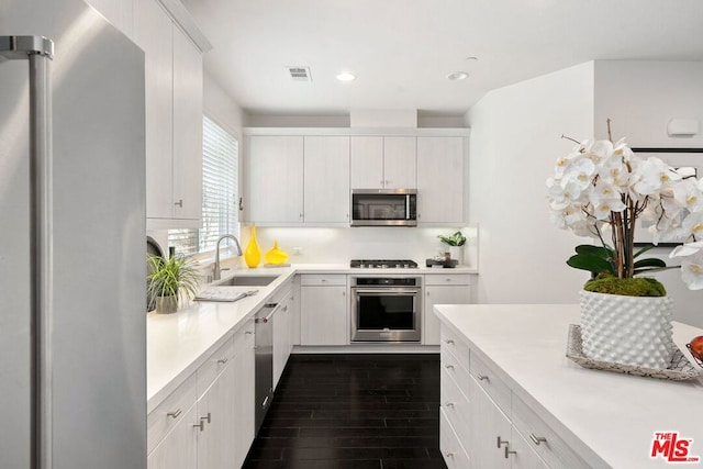 kitchen with appliances with stainless steel finishes, dark hardwood / wood-style flooring, white cabinets, and sink