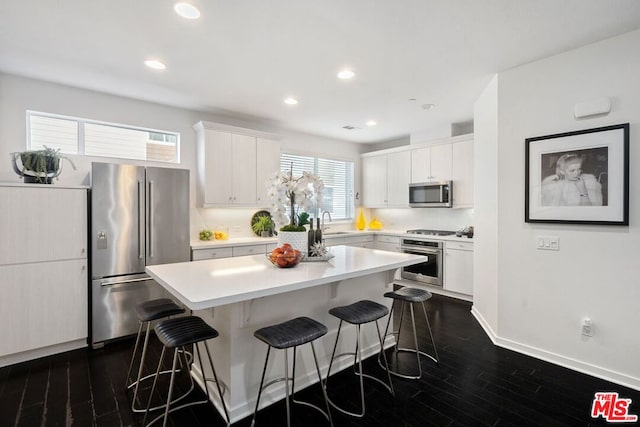 kitchen featuring a kitchen breakfast bar, stainless steel appliances, dark hardwood / wood-style flooring, a kitchen island, and white cabinets