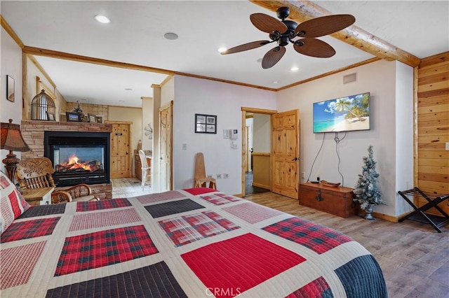 bedroom featuring hardwood / wood-style floors, beamed ceiling, ceiling fan, ornamental molding, and a fireplace