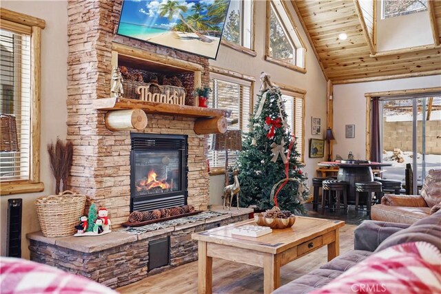 living room featuring a wealth of natural light, high vaulted ceiling, wood ceiling, and a stone fireplace