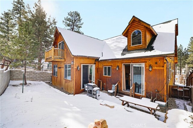 snow covered back of property featuring a balcony