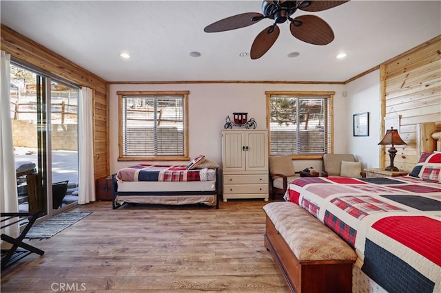 bedroom with ceiling fan, access to exterior, light hardwood / wood-style floors, crown molding, and wooden walls