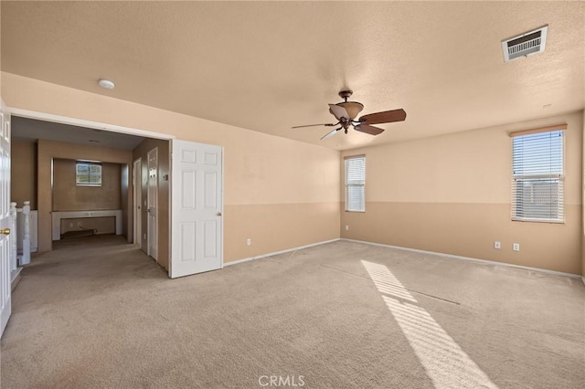 empty room with light colored carpet, ceiling fan, and a wealth of natural light