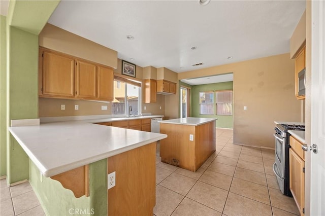 kitchen featuring kitchen peninsula, stainless steel range with gas cooktop, a kitchen island, light tile patterned flooring, and sink